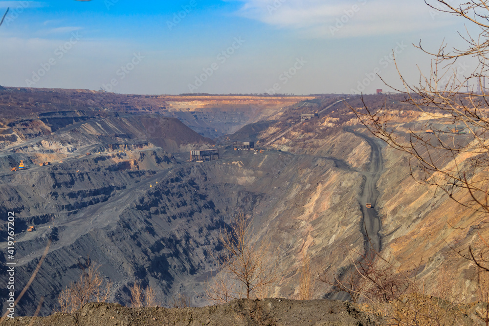 Fototapeta premium Huge iron ore quarry with working dump trucks and excavators