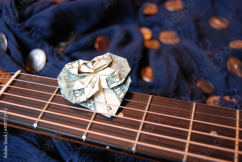 Dollar bill origami heart tucked into guitar strings with coins in background