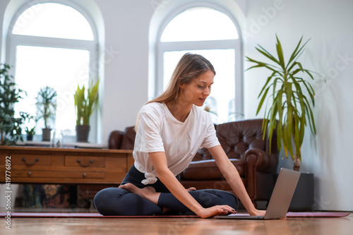 Calm portrait of a sportswoman dressed in activewear using her laptop and sitting on floor. Domestic sportive lifestyle.