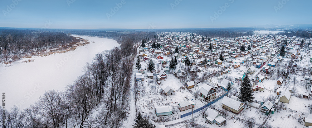 Traditional Russian dacha village near river and forest in winter, aerial view