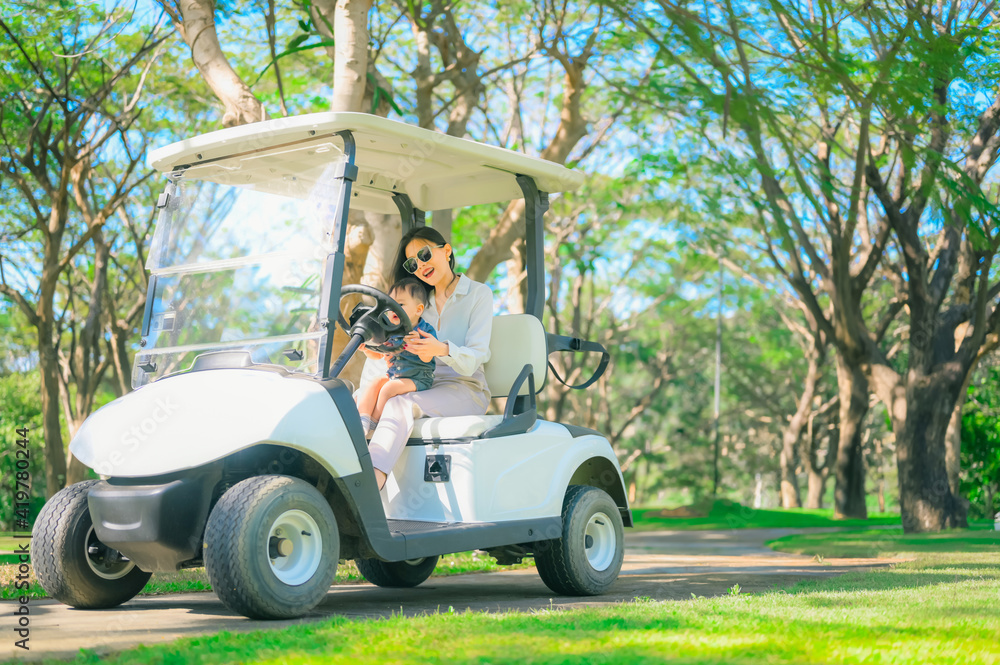 Naklejka premium A woman is sitting at the wheel of a golf car, the son is sitting next to the passenger seat.