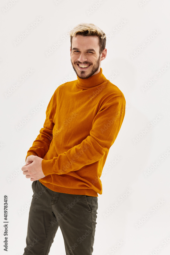 happy blond guy in an orange sweater and trousers laughs on a light background happy blond guy in an orange sweater and trousers laughs on a light background
