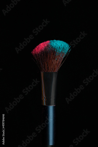 Make-up brush with pink and blue powder isolated on black background