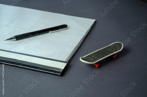 Skateboard finger, folder for papers and pencil on gray table.