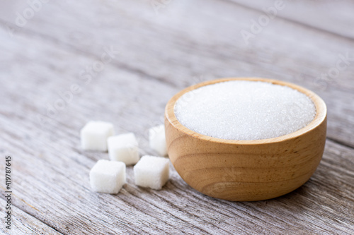 White sand sugar in wooden bowl and wooden spoon and cube sugar on wood table background.