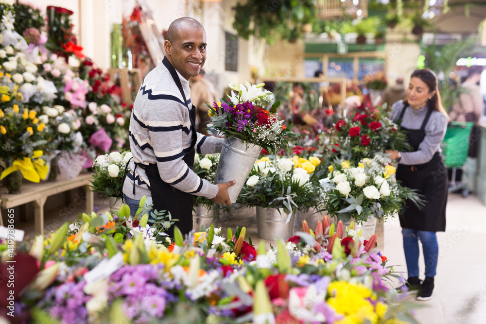 Fototapeta premium Florist man in apron creates bouquets in flower shop