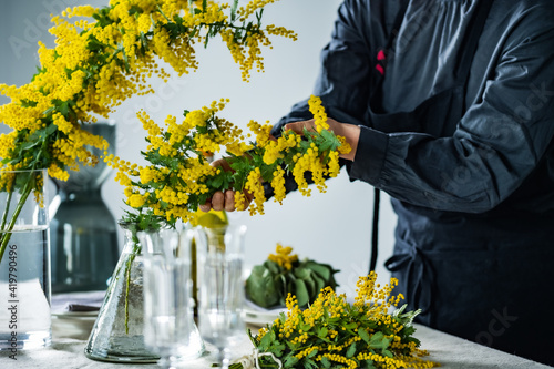 Woman placing bouquet of mimosa on a dining table. 