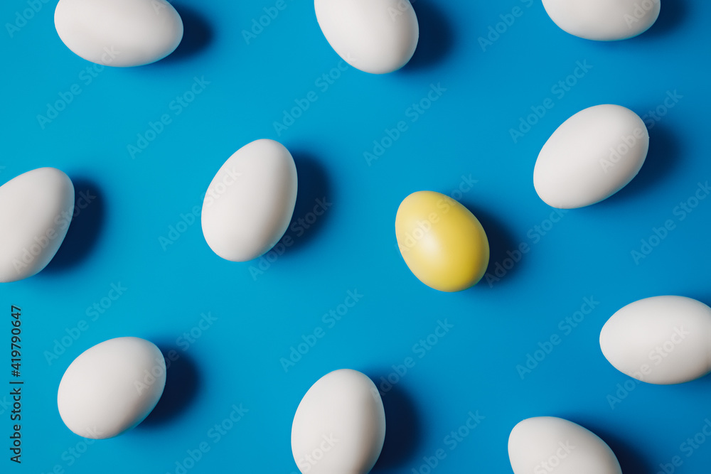 One yellow egg among white eggs on vibrant blue background. Minimal Easter or food layout. Creative concept of individuality, exclusivity, better choice. Flat lay, top view. One yellow egg among white eggs on vibrant blue background. Minimal Easter or food layout. Creative concept of individuality, exclusivity, better choice. Flat lay, top view.
