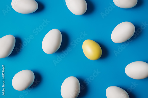 One yellow egg among white eggs on vibrant blue background. Minimal Easter or food layout. Creative concept of individuality  exclusivity  better choice. Flat lay  top view.