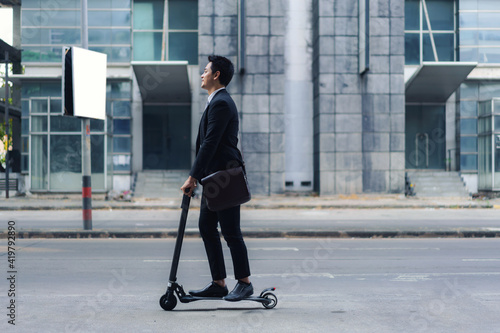 Wallpaper Mural Asian businessman riding an electric scooter on the city streets to go to work in the morning. Daily commute that best reflect the working world of today. Torontodigital.ca