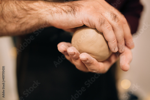 Male hands are holding a clay ball. Preparing clay for sculpting a pot on a potter's wheel