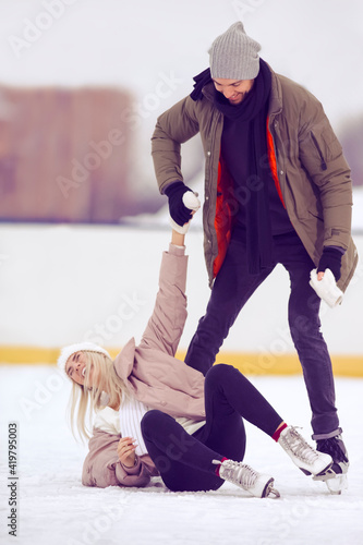 Happy Caucasian Couple in Winter With Ice Skates Skating and Having Fun Together While Woman Falling on Ice Outdoors.