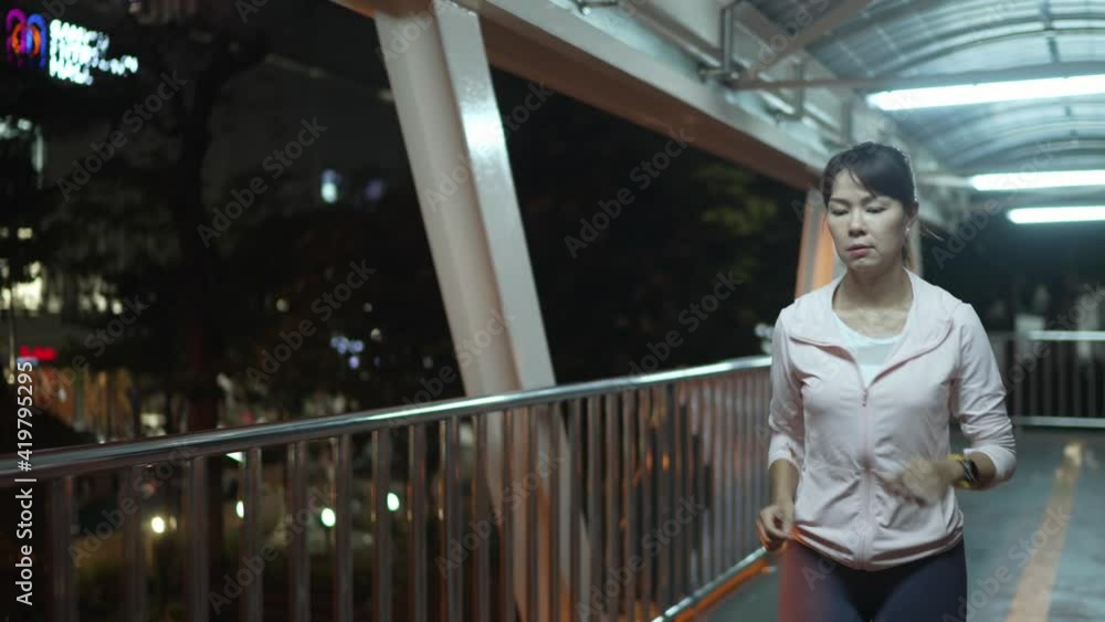Slow-motion,Font Follow Camera View.Female athlete wearing a pink hoodie. Practice jogging Running through the overpass at night every day, the city streets with many lights.Night City run Concept. Slow-motion,Font Follow Camera View.Female athlete wearing a pink hoodie. Practice jogging Running through the overpass at night every day, the city streets with many lights.Night City run Concept.