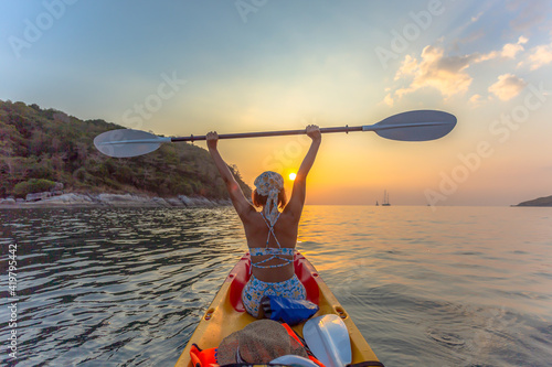 A female tourist wearing a bikini sits on a canoe. .And raise a canoe paddle in the sunset at Yanui Beach Phuket Thailand.