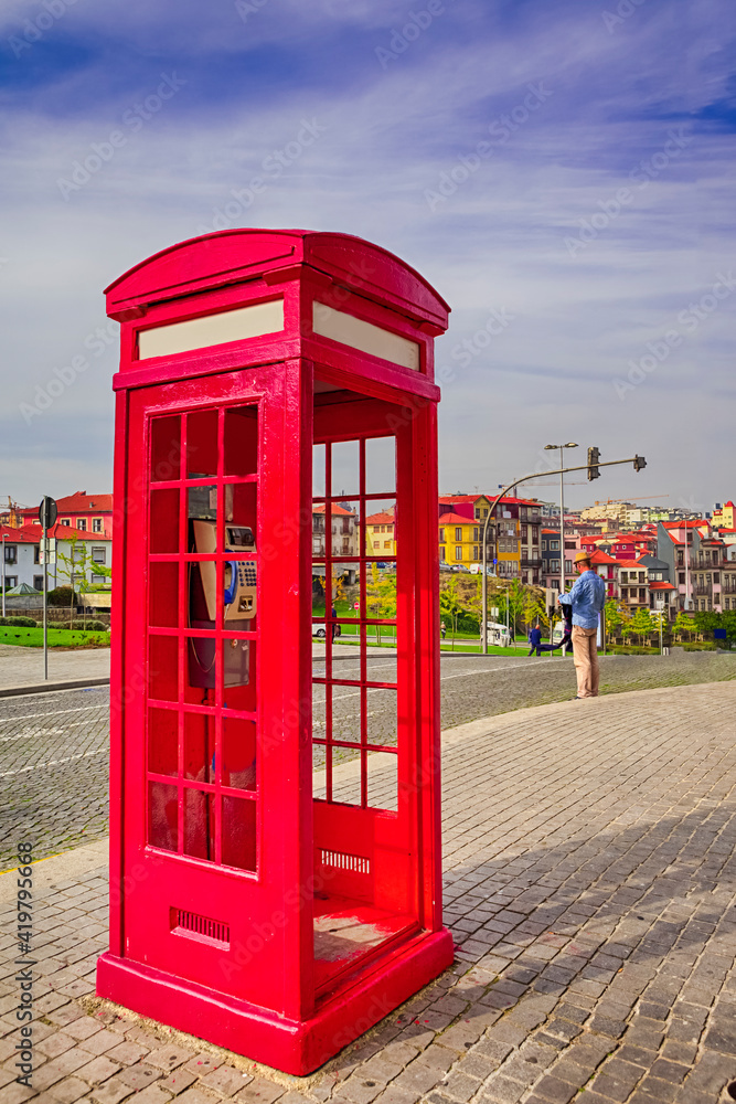 Porto Travel Destinations. Traditional Red Public Call Box in Porto City in Portugal At Daytime with Line of Houses on Background Porto Travel Destinations. Traditional Red Public Call Box in Porto City in Portugal At Daytime with Line of Houses on Background