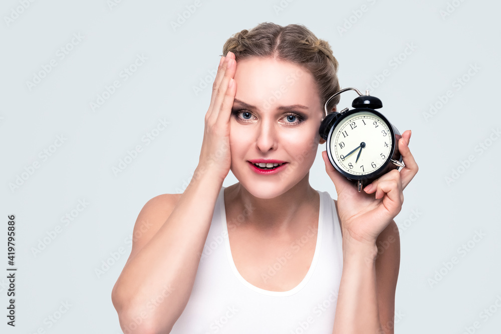 Portrait of Young Stressfull Caucasian Female With Alarm Clock And Lifted Hand on Face. Portrait of Young Stressfull Caucasian Female With Alarm Clock And Lifted Hand on Face.