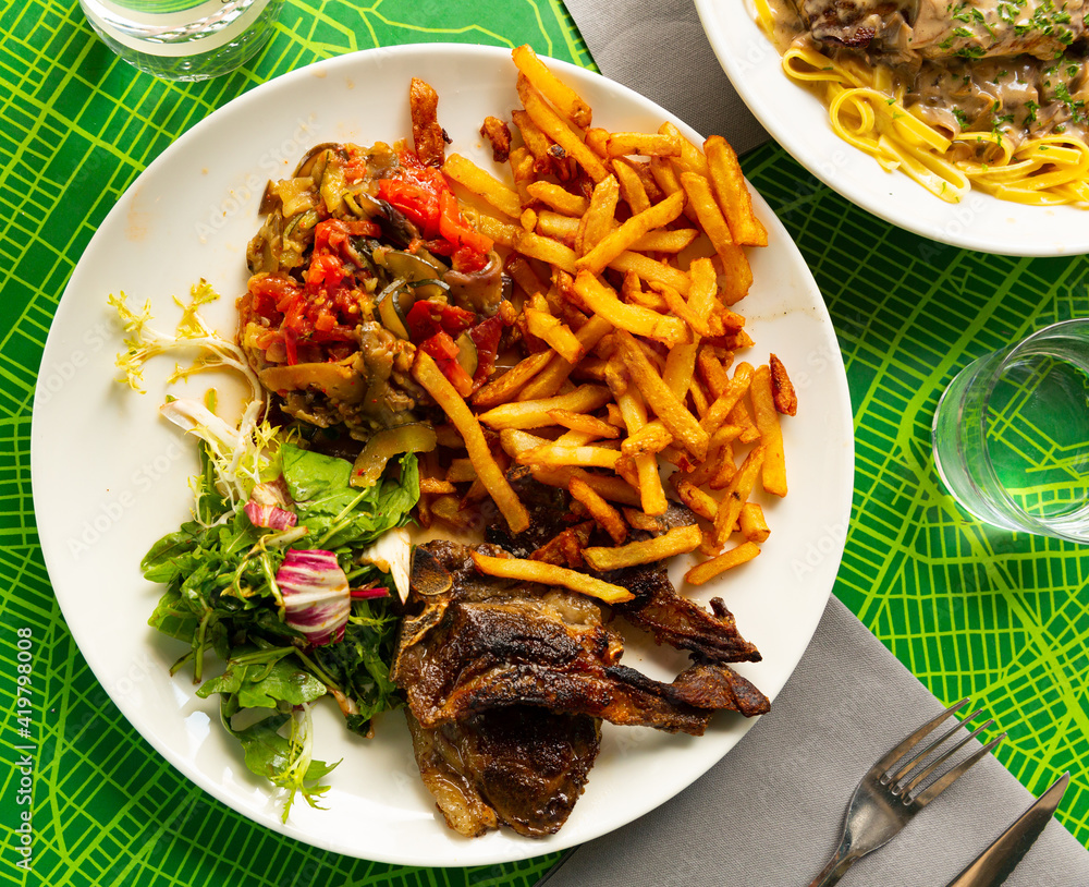 Portion of barbecued lamb ribs with french fries and vegetable garnish. High quality photo