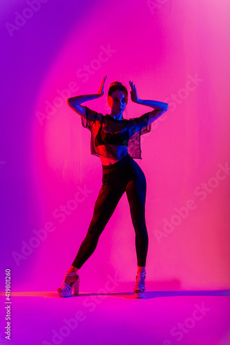 Beautiful young woman wearing sexy high heels and black clothes while dancing in pole dance studio