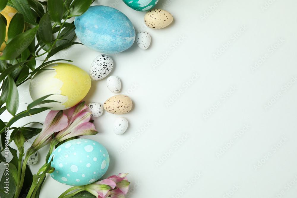 Easter eggs and beautiful flowers on white background, space for text