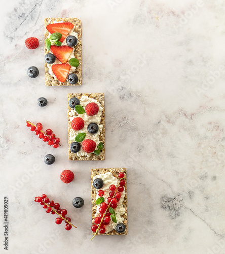 Snack with rye oats crispbread, cottage cheese, and fresh berries on a marble table.