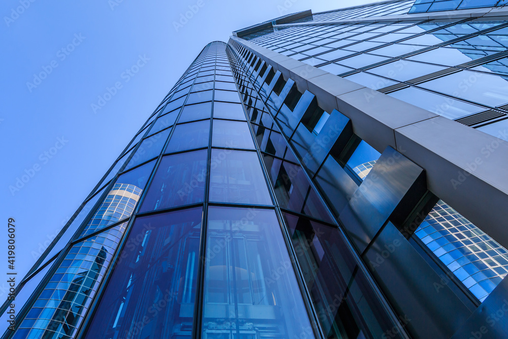 Obraz premium Glass facade of a high-rise in Frankfurt. View along one of a skyscraper with reflections in the windows. House of the finance and business district with blue sky and sunshine