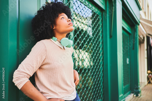 Fotografie Afro-haired woman with headphones leaning against green wall