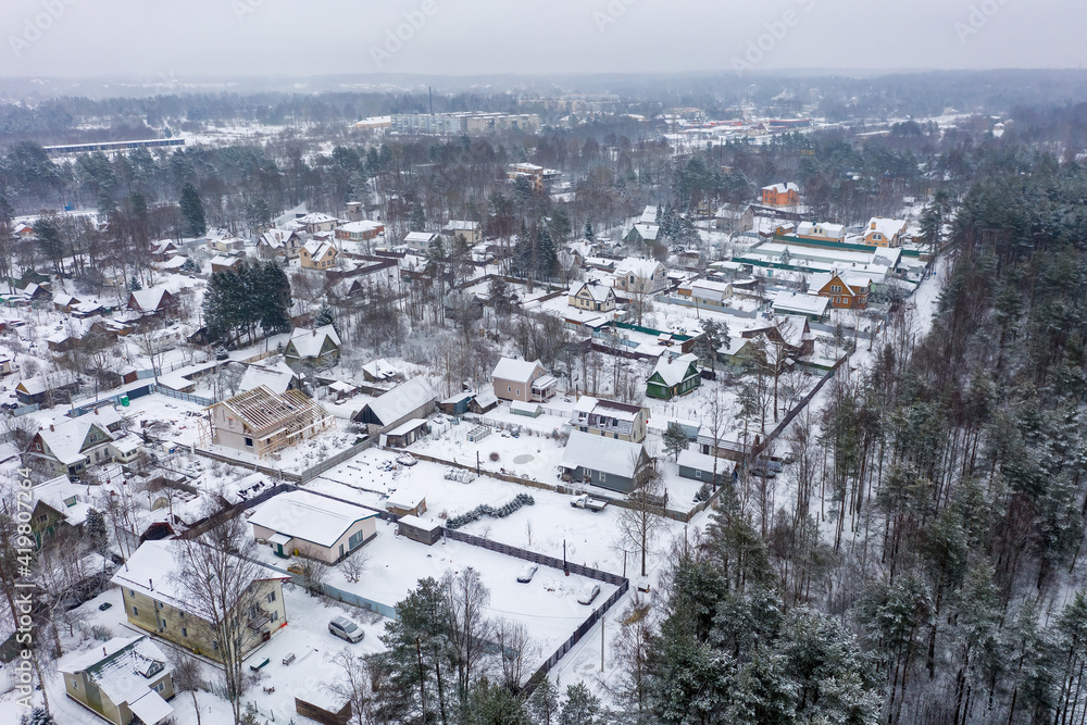Aerial view of a snow-covered village. Winter rural landscape. Top view of the streets, houses and trees. Cold snowy winter weather. Snowfall. Snow on the roofs. Toksovo, Leningrad region, Russia.