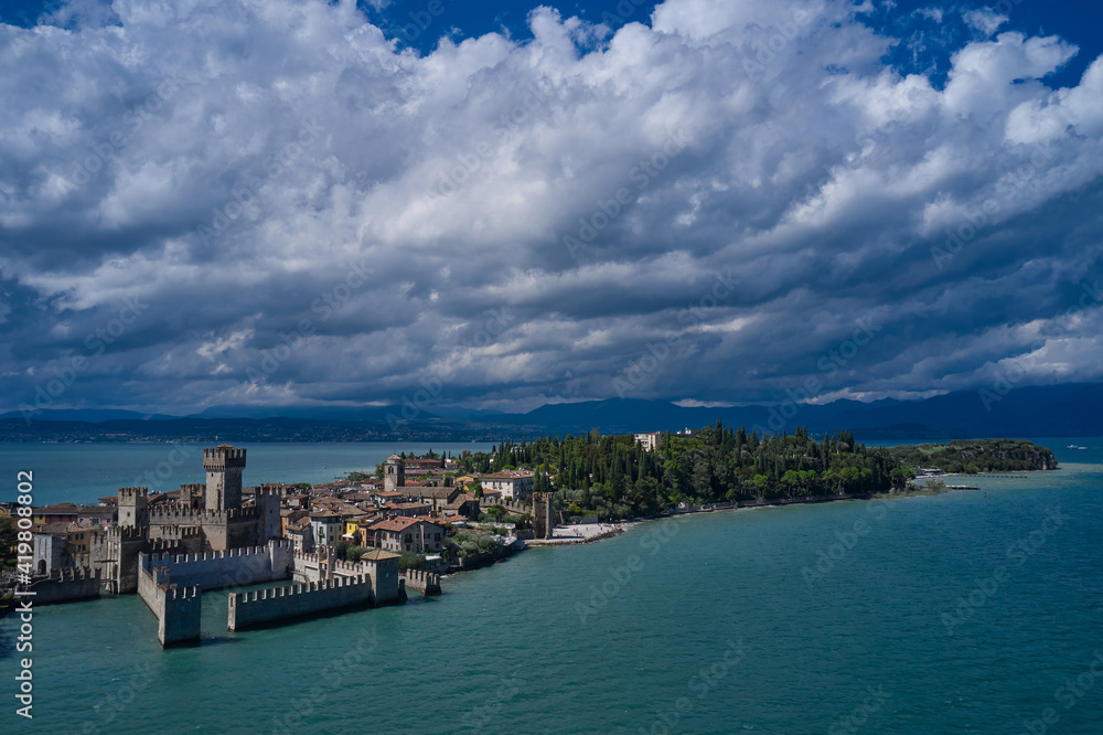 Rocca Scaligera Castle in Sirmione. Cumulus clouds over the island of Sirmione. Panoramic view at high altitude. Aerial photography with drone. Aerial view on Sirmione sul Garda. Italy, Lombardy.
