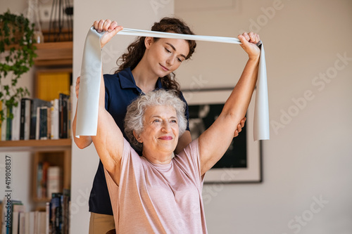 Senior patient doing exercise with elastic band at home with personal trainer