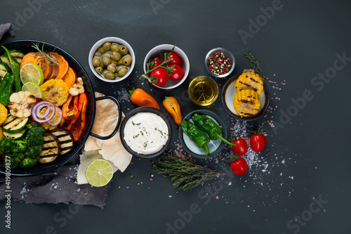 Grilled assorted vegetables in cast iron pan on black background.