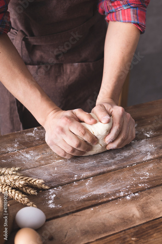 Baker male hand kneading or making dough and bakery ingredients for homemade bread cooking on table