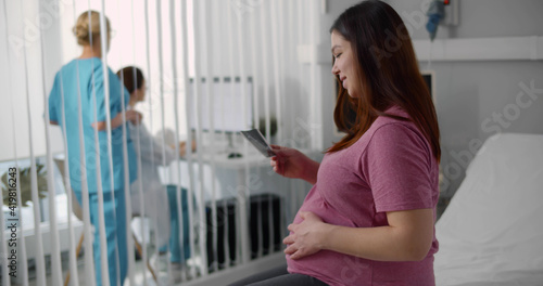 Free Download Young pregnant woman looking at ultrasound image sitting at bed in hospital - GFXLoad