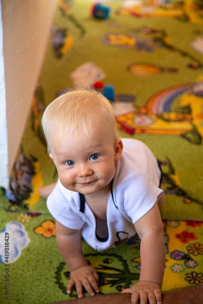 Beautiful blonde toddler crawls on all fours on the floor in summer and smiles very cute Beautiful blonde toddler crawls on all fours on the floor in summer and smiles very cute