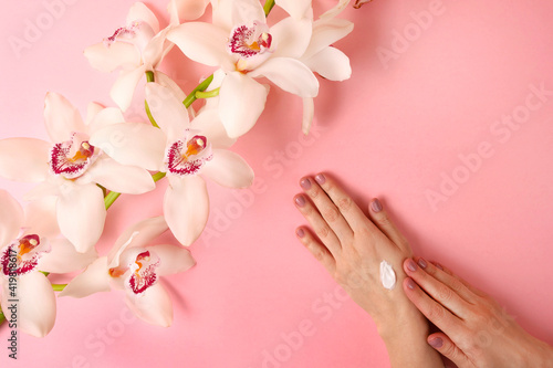 Woman applyiing cosmetic cream on her hands on rose background with orhid flower. Home spa  beauty and treatment concept. Flat lay  top view