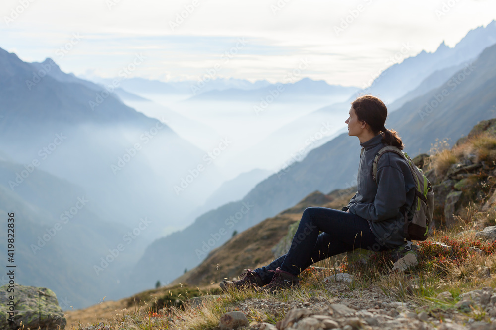 Woman with backpack enjoying sunset on peak of foggy mountain. Tourist traveler on background view mockup. Hiker looking sunlight in trip in Italy country mock up text. Alpine mountain