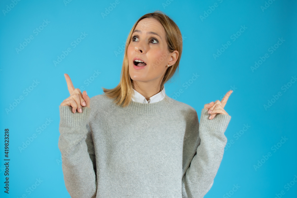 Portrait of a happy young woman pointing fingers up at copy space isolated over blue background Portrait of a happy young woman pointing fingers up at copy space isolated over blue background