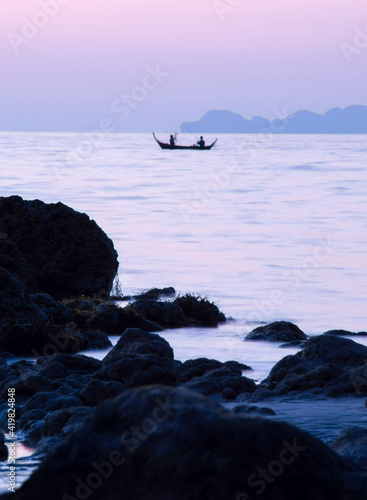 Two fisherman fishing in front of rocky beach at purple dusk