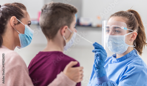 Mom holds her son as medical worker takes sample from his nose during coronavirus pandemic testing