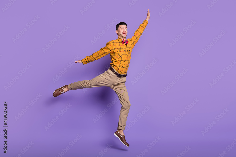 Full length photo of cute sweet young guy dressed checkered shirt jumping arms sides isolated purple color background
