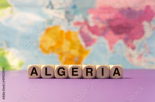 The word Algeria written with wooden dices in front of a purple background and a geographic map photo