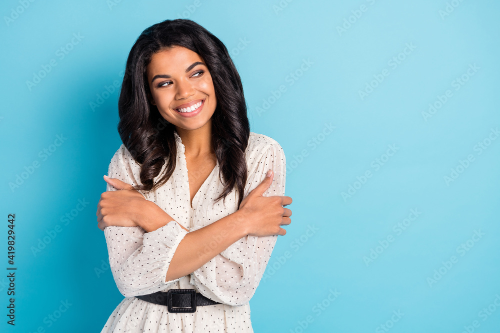 Fototapeta premium Portrait of attractive cheerful curious girl hugging herself looking aside copy space isolated over bright blue color background