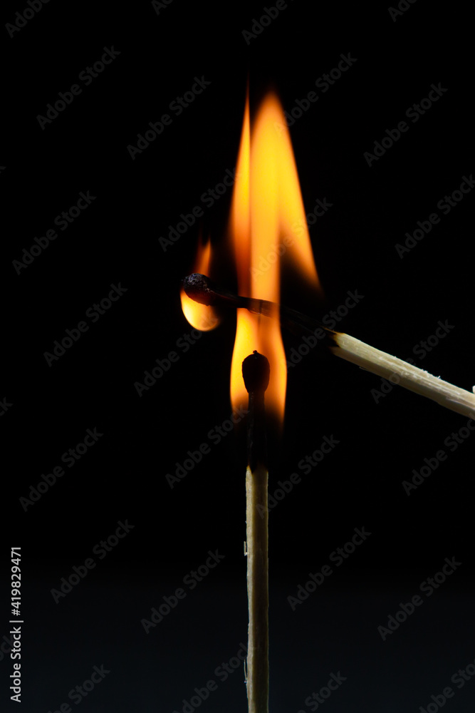 Burning match on a black background. A match sets fire to another match against a dark background. Burning in the dark
