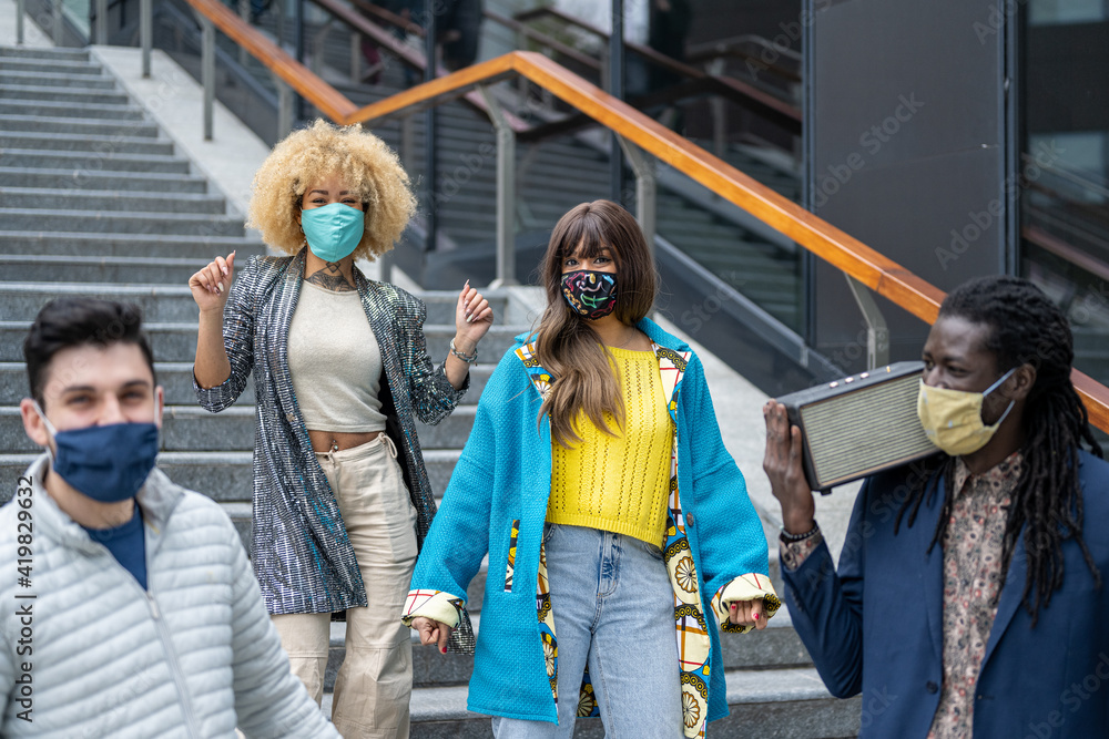 group of young people dancing in the city, social distancing and protection with facemask, millennials having fun with a party in the street