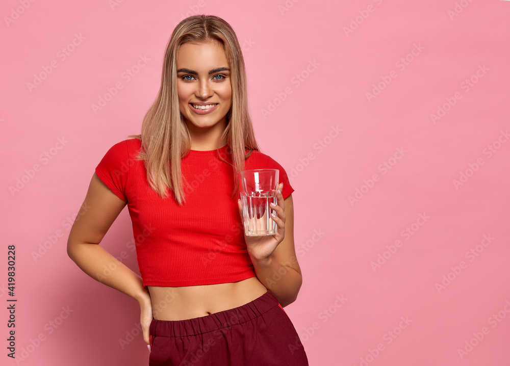 Smiling blonde woman in sport suit holding a glass of water isolated on pastel background Smiling blonde woman in sport suit holding a glass of water isolated on pastel background