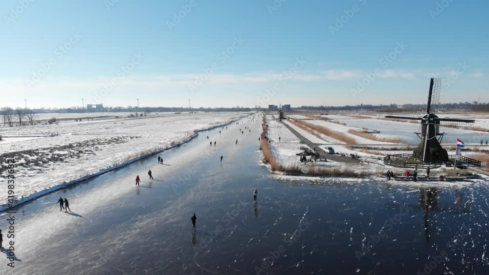 Dutch people winter ice skating on frozen canal near old windmill, aerial view Dutch people winter ice skating on frozen canal near old windmill, aerial view