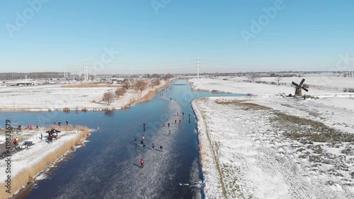 Aerial: people ice skating on frozen Netherlands canal near old windmill photo