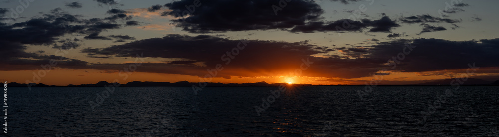 panorama of a scenic and colorful sunset over the ocean and silhouette of mountains on the shore behind