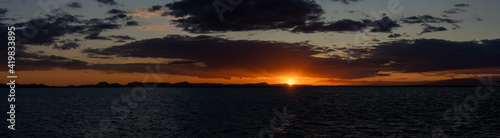 panorama of a scenic and colorful sunset over the ocean and silhouette of mountains on the shore behind © makasana photo