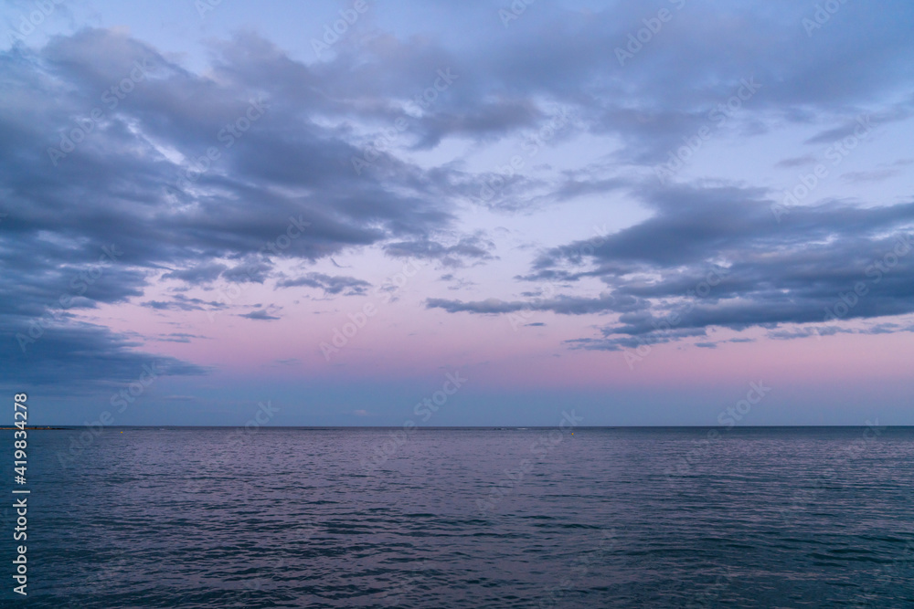 background landscape of calm dark blue ocean water under an expressive sky with clouds at sunset