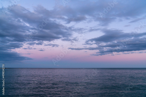 background landscape of calm dark blue ocean water under an expressive sky with clouds at sunset